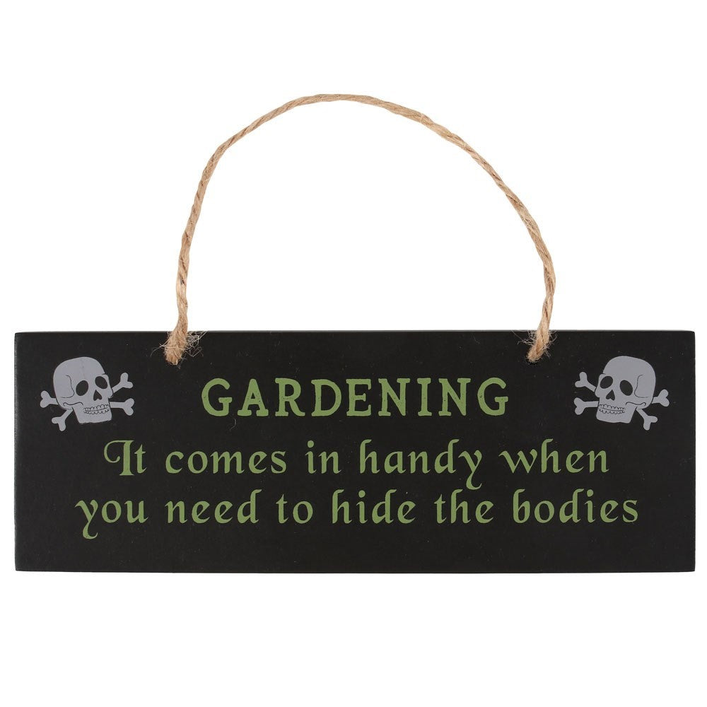 A wooden sign with a rope for hanging from a nail. The title reads “Gardening” with two skull-and-crossbones on either side. Below is the caption “It comes in handy when you need to hide the bodies.”